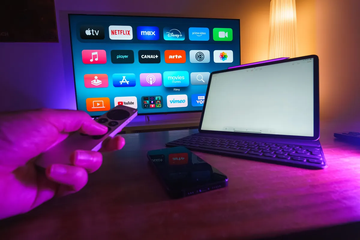 Home entertainment setup with a smart TV displaying streaming apps, a tablet, and a smartphone on a coffee table, representing the Apple TV IPTV streaming experience across multiple devices