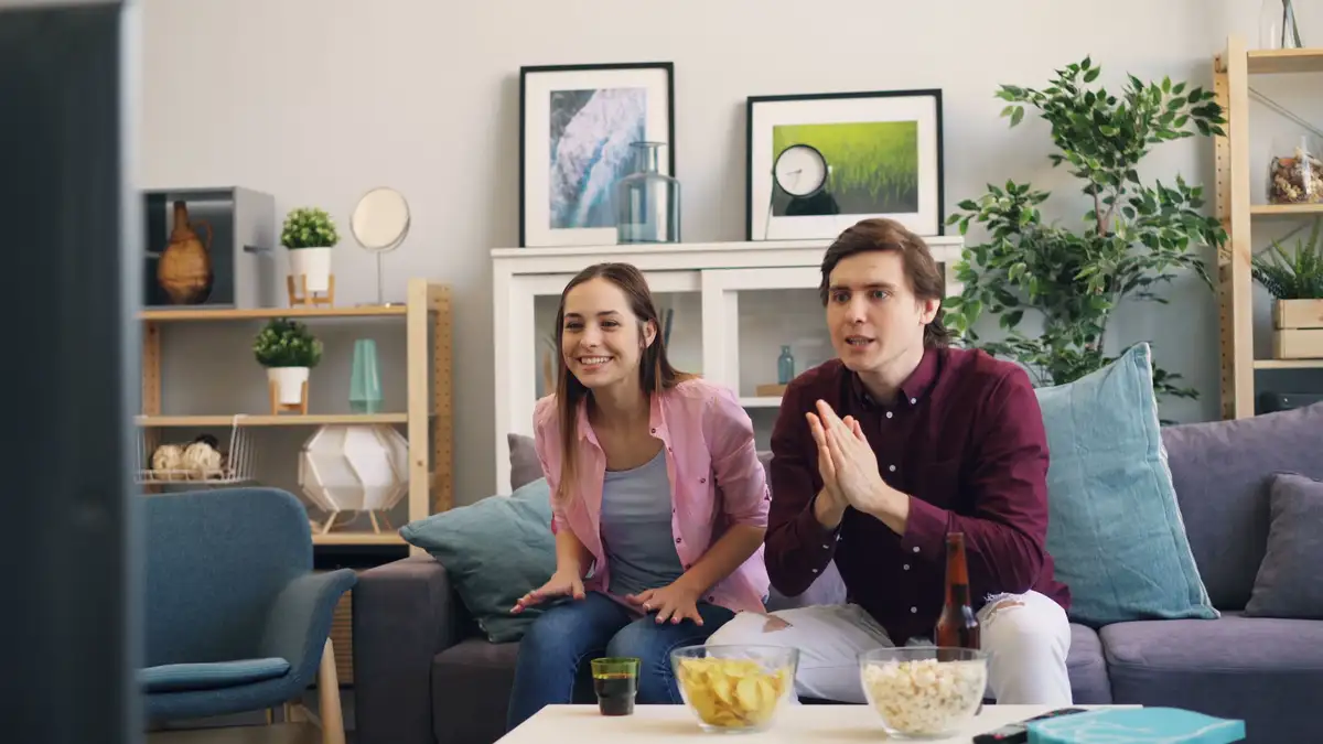 Happy couple watching television together on a comfortable sofa in a cozy living room, showcasing the final optimized Apple TV IPTV streaming setup experience